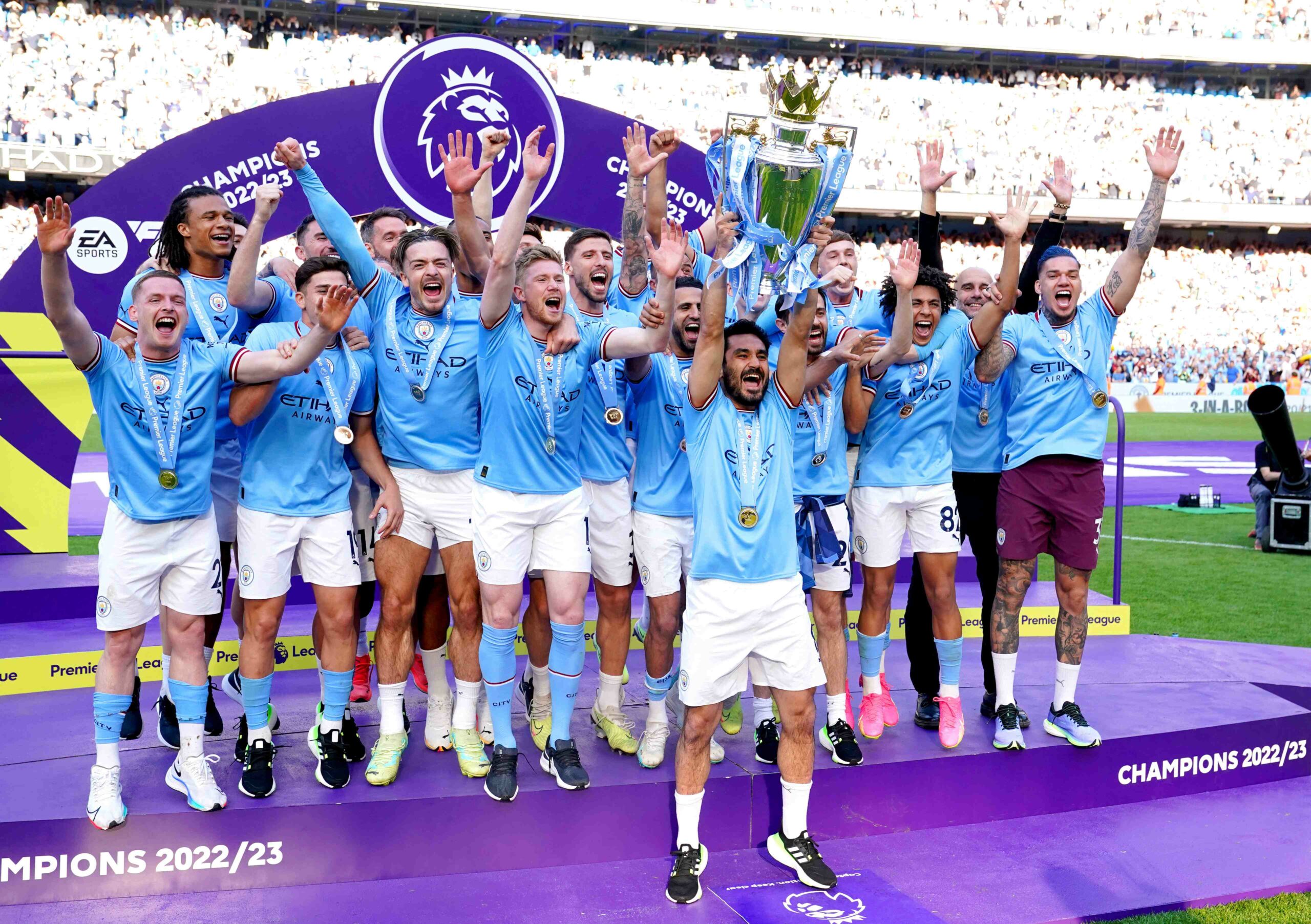 Manchester City players and staff celebrating their victory with the EPL trophy in front of jubilant fans at the Etihad Stadium, marking their triumph in the 2022-23 season.