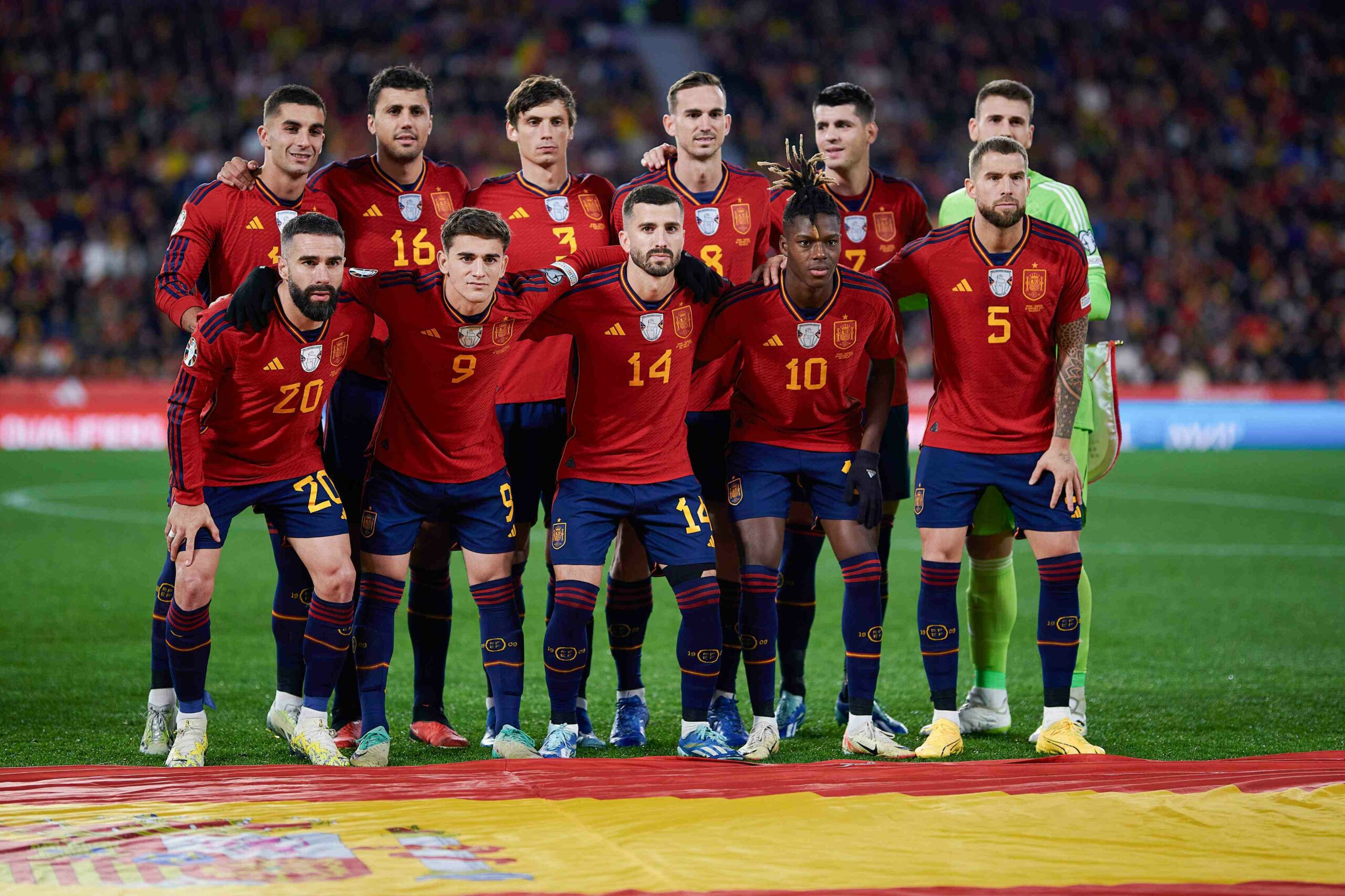 The Spanish national football team, dressed in their iconic red and gold uniforms, poses for a group photo on the pitch before the start of their Euro 2024 qualification game, exuding a blend of determination and camaraderie.